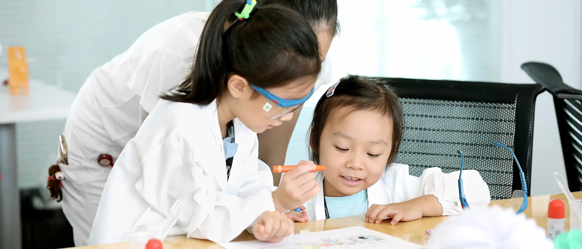 طفلان وامرأة ترتدي معطف المختبر يلونان صورة على طاولة
