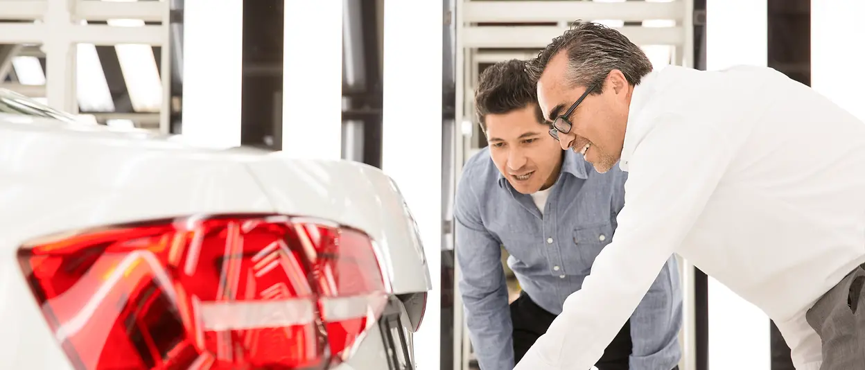 Two men are examining the backside of a white car.